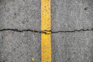 Closeup photo of an asphalt road with a yellow line and a big crack going across it.