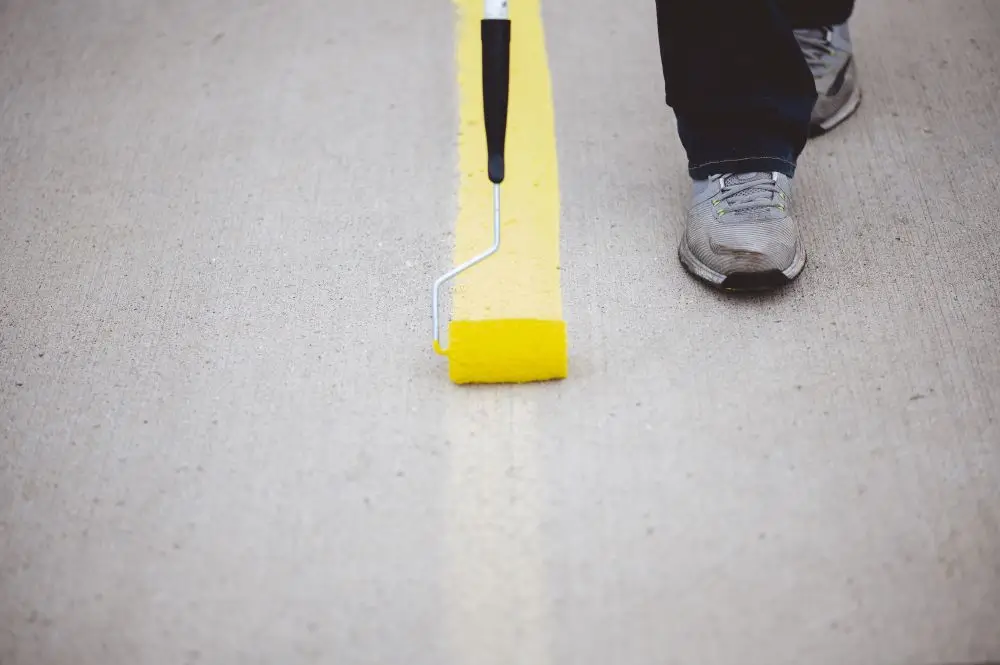 Photo of a persons feet repainting parking lines with a roller.